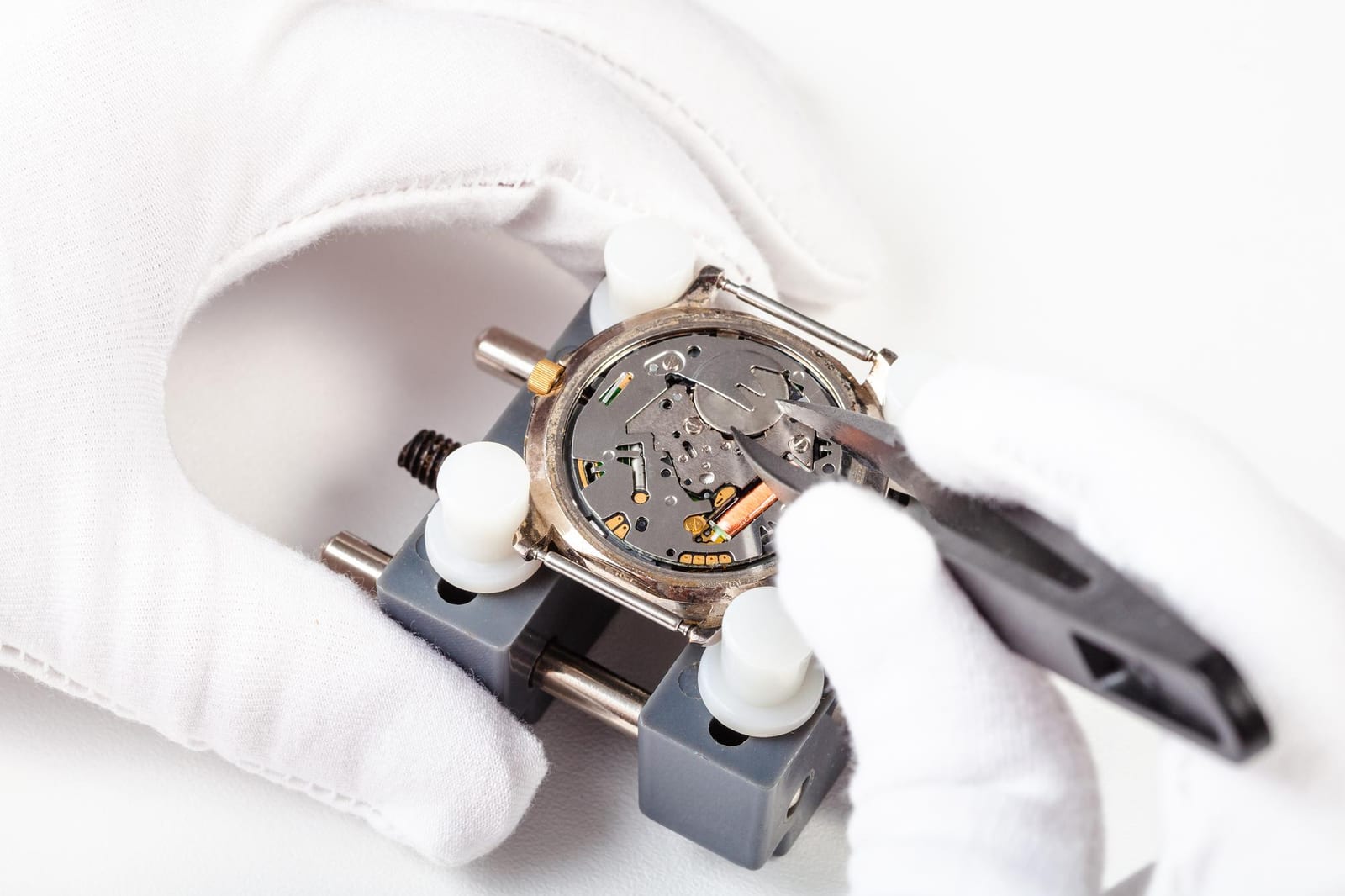 Mani guantate che regolano con una pinzetta il movimento al quarzo aperto di un orologio da polso
